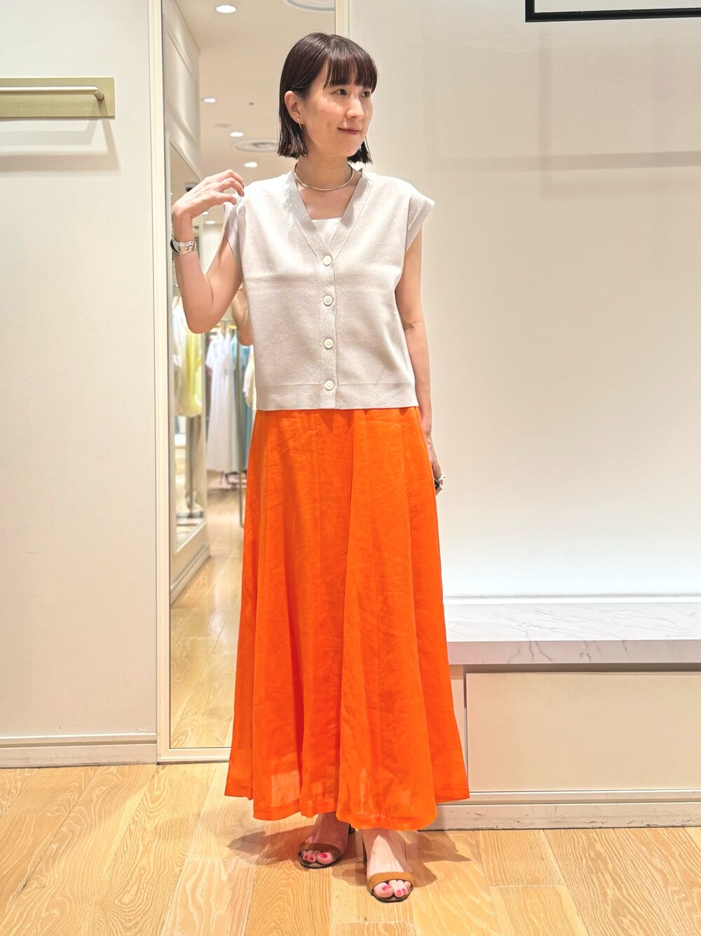 ベージュ系のベスト、ホワイト系のタンクトップ、オレンジ系のスカートを着用したレディースの夏コーディネートの1枚目の写真