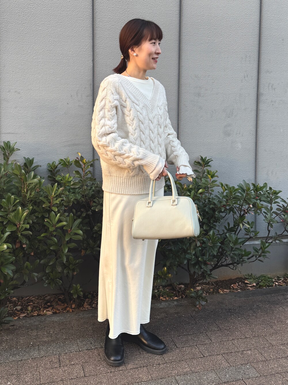 ホワイト系のニット/セーター、ホワイト系のTシャツ/カットソー、グリーン系のショルダーバッグを着用したレディースの冬コーディネートの1枚目の写真