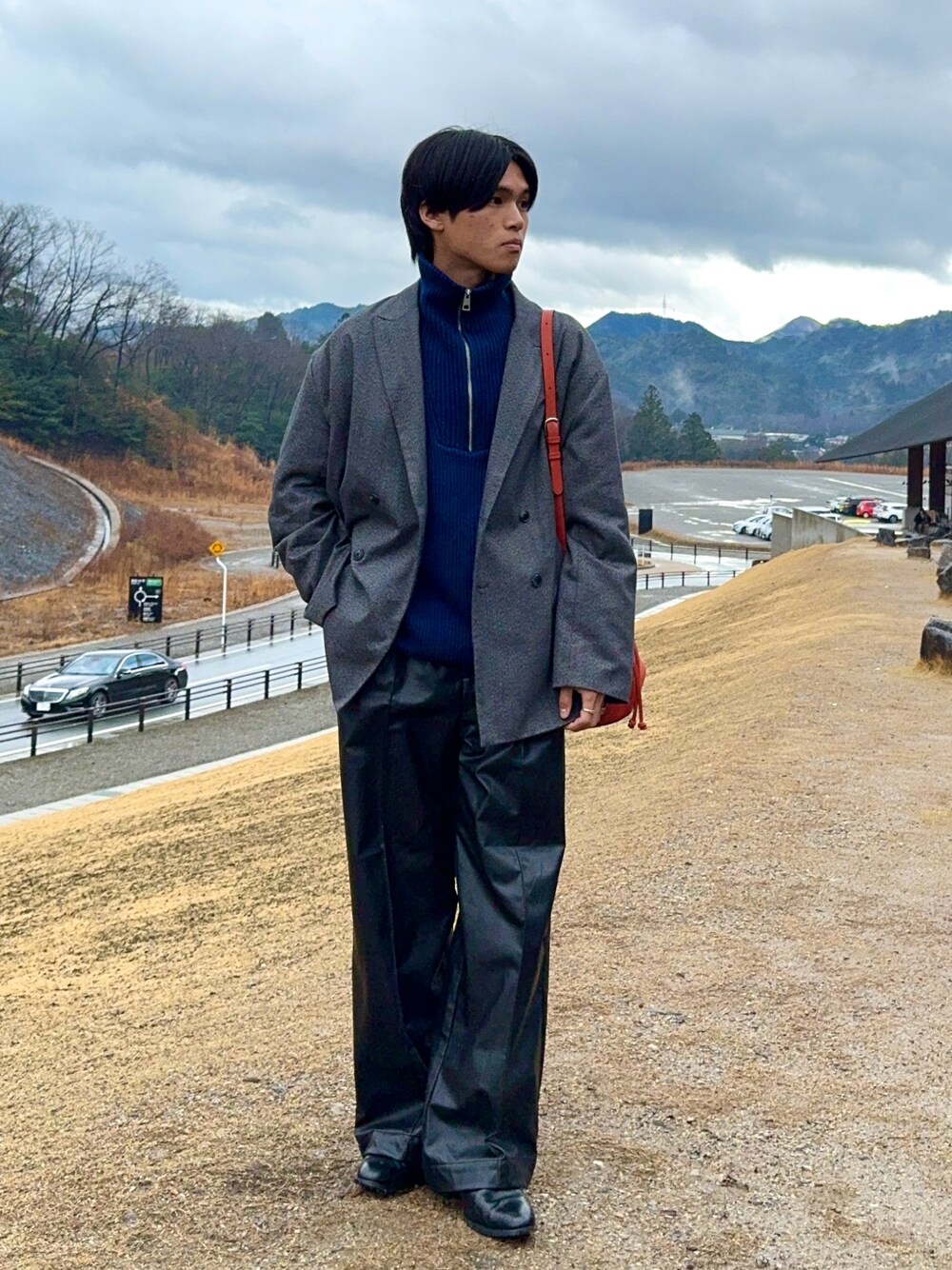 ブラック系のその他パンツ、ブラック系のブーツ、オレンジ系のバッグを着用したメンズの春コーディネートの1枚目の写真