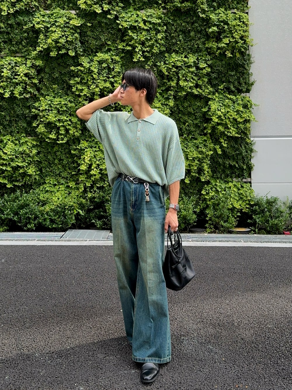 ブルー系のデニムパンツ、ブラック系のバッグ、グリーン系のポロシャツを着用したメンズの夏コーディネートの1枚目の写真