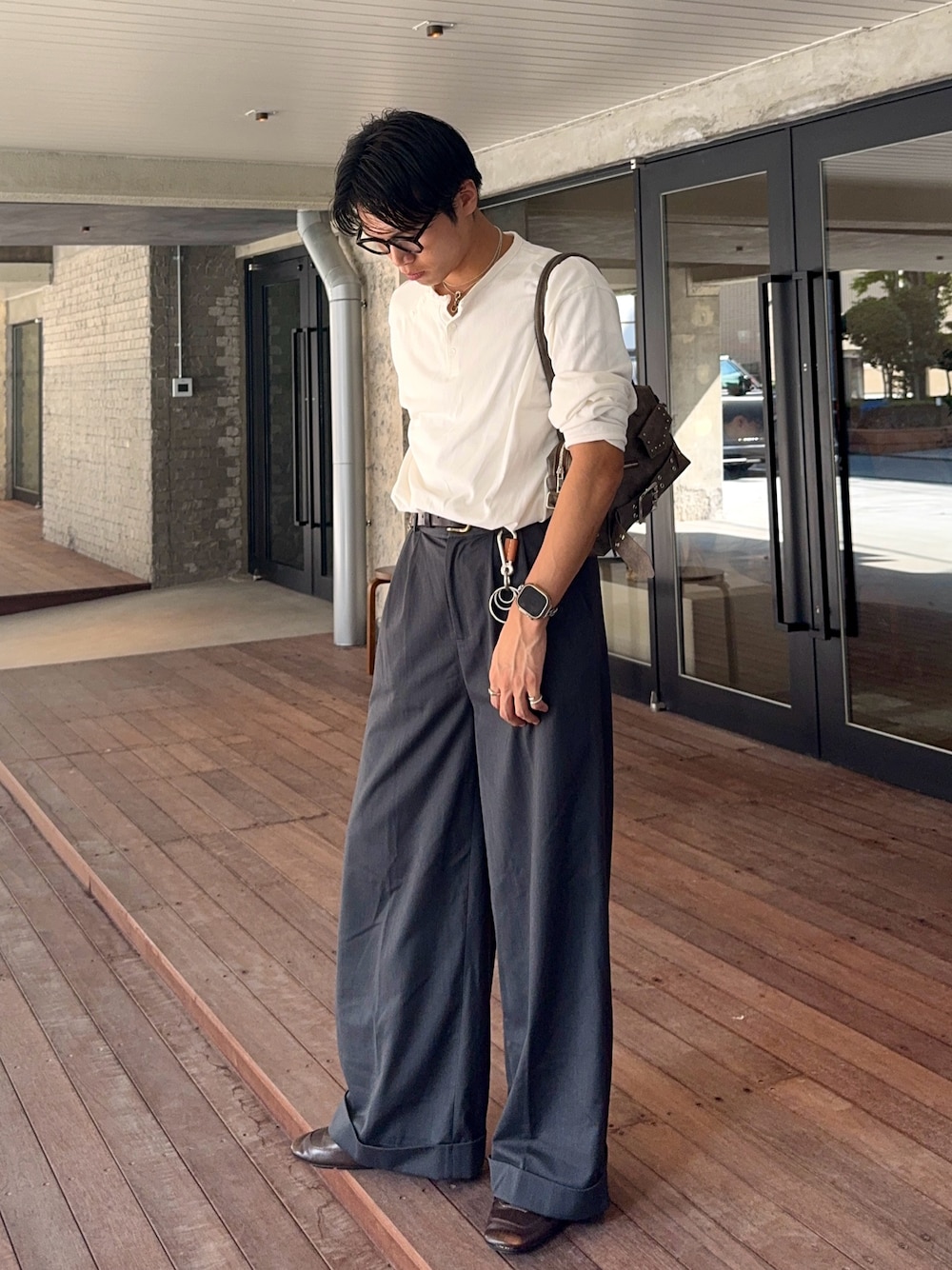 グレー系のスラックス、ホワイト系のTシャツ/カットソー、ブラウン系のショルダーバッグを着用したメンズの秋コーディネートの1枚目の写真