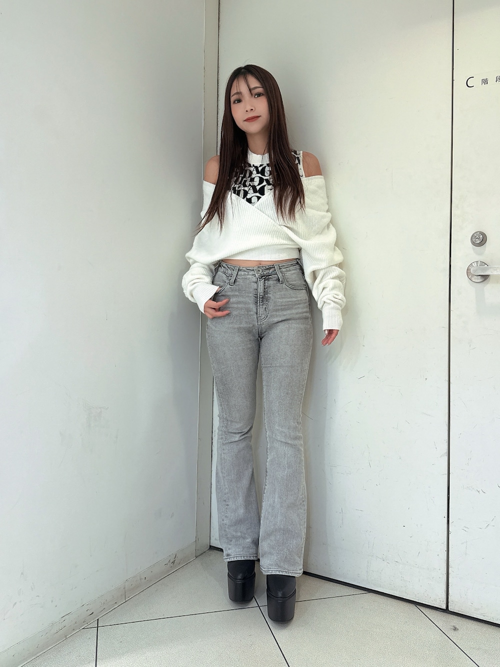 グレー系のデニムパンツ、ブラック系のブーツ、ホワイト系のニット/セーターを着用したレディースの秋コーディネートの1枚目の写真