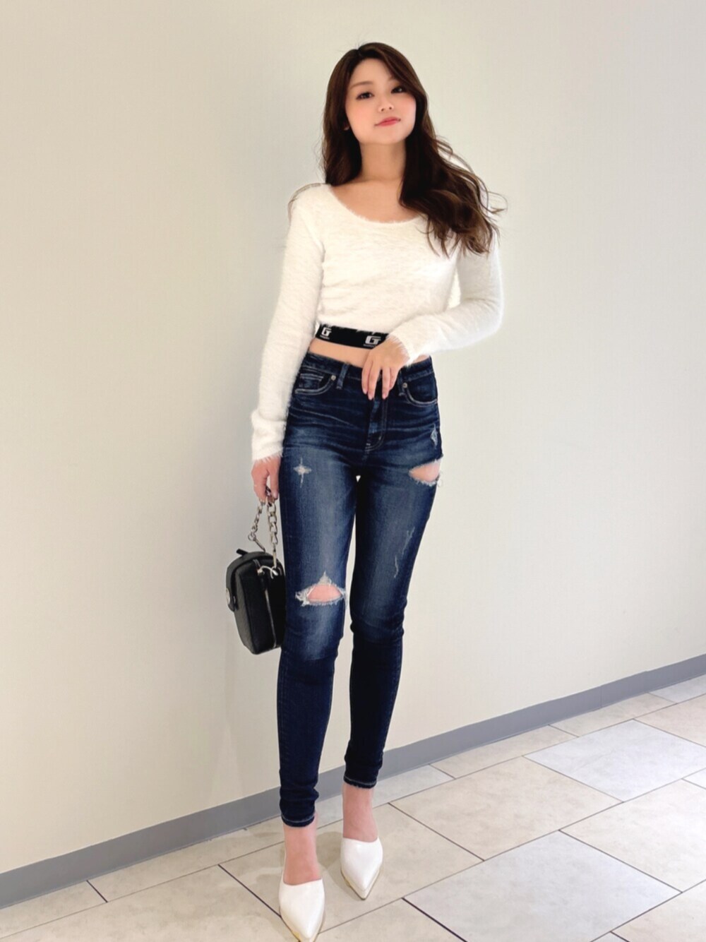 ホワイト系のパンプス、ブルー系のデニムパンツ、ブラック系のショルダーバッグを着用したレディースの冬コーディネートの1枚目の写真