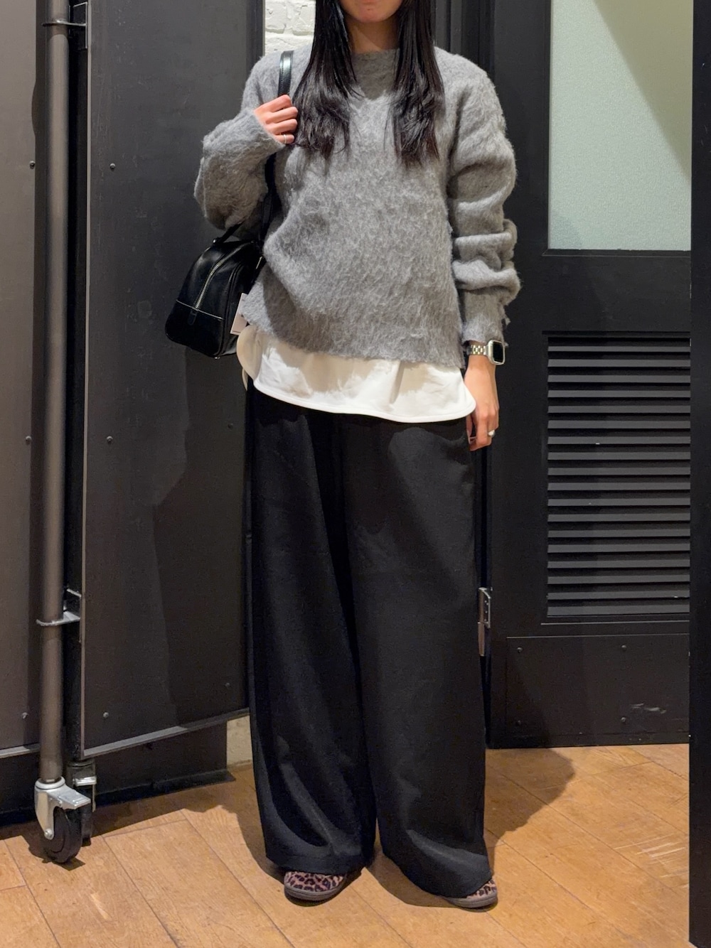 ブラック系のスラックス、ホワイト系のTシャツ/カットソー、グレー系のニット/セーターを着用したレディースの冬コーディネートの1枚目の写真