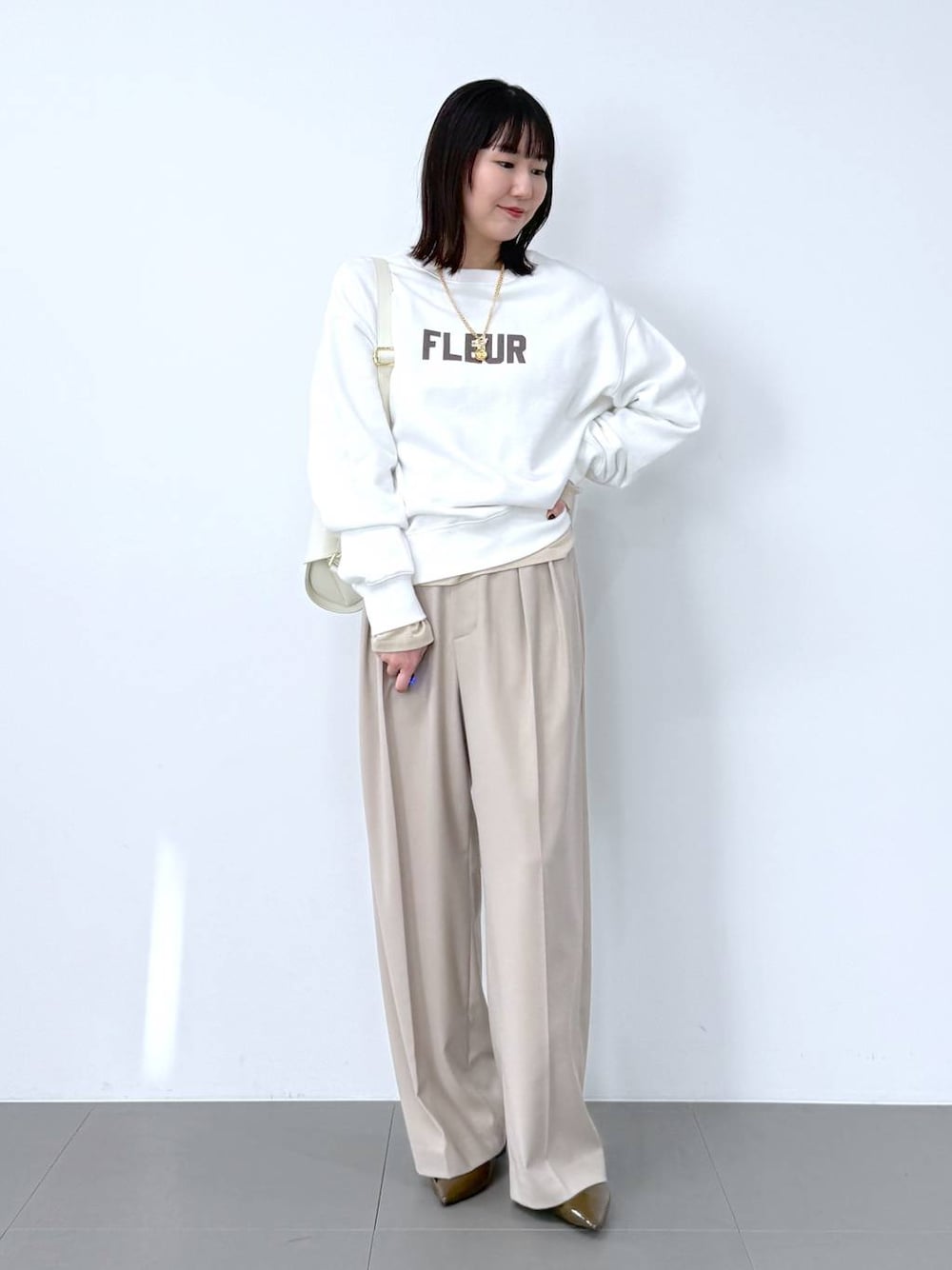 ホワイト系のスウェット、ホワイト系のショルダーバッグ、ベージュ系のスラックスを着用したレディースの冬コーディネートの1枚目の写真