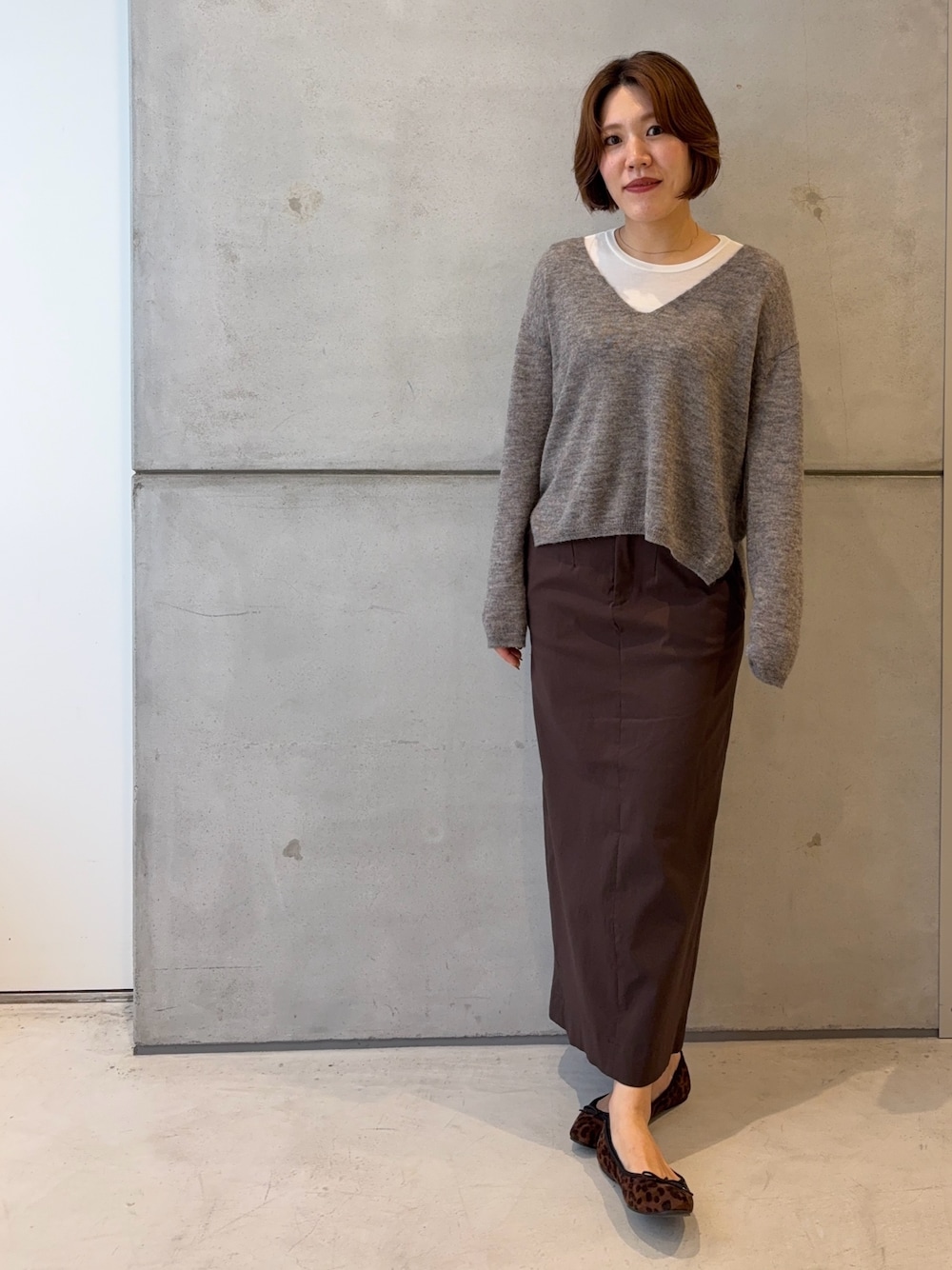 ホワイト系のTシャツ/カットソー、グレー系のニット/セーター、ブラウン系のスカートを着用したレディースの秋コーディネートの1枚目の写真
