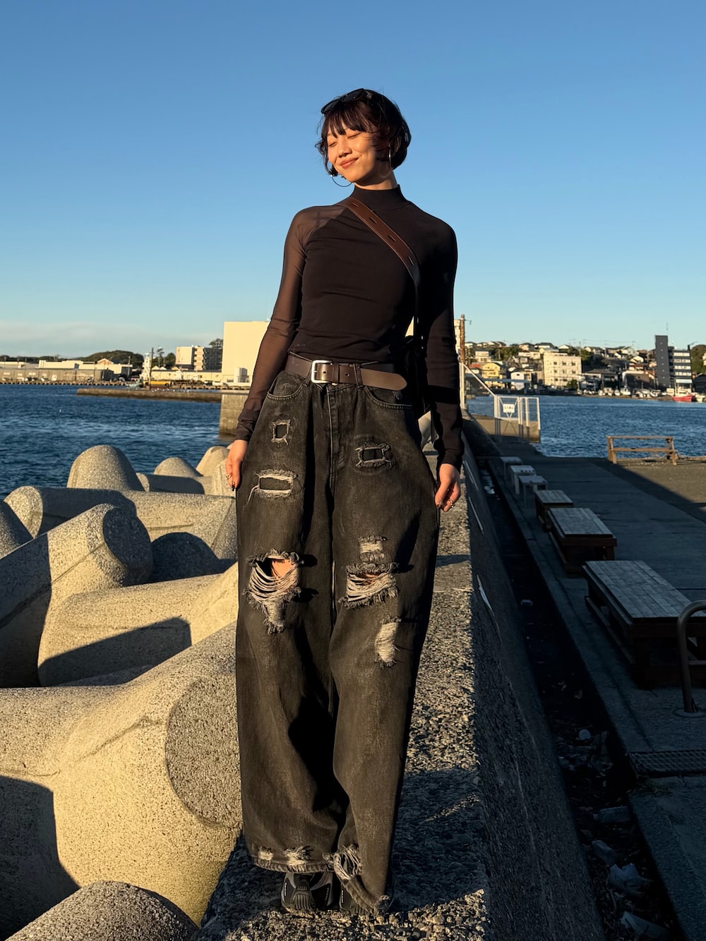 シルバー系のスニーカー、ブラック系のデニムパンツ、ブラウン系のショルダーバッグを着用したレディースの秋コーディネートの1枚目の写真