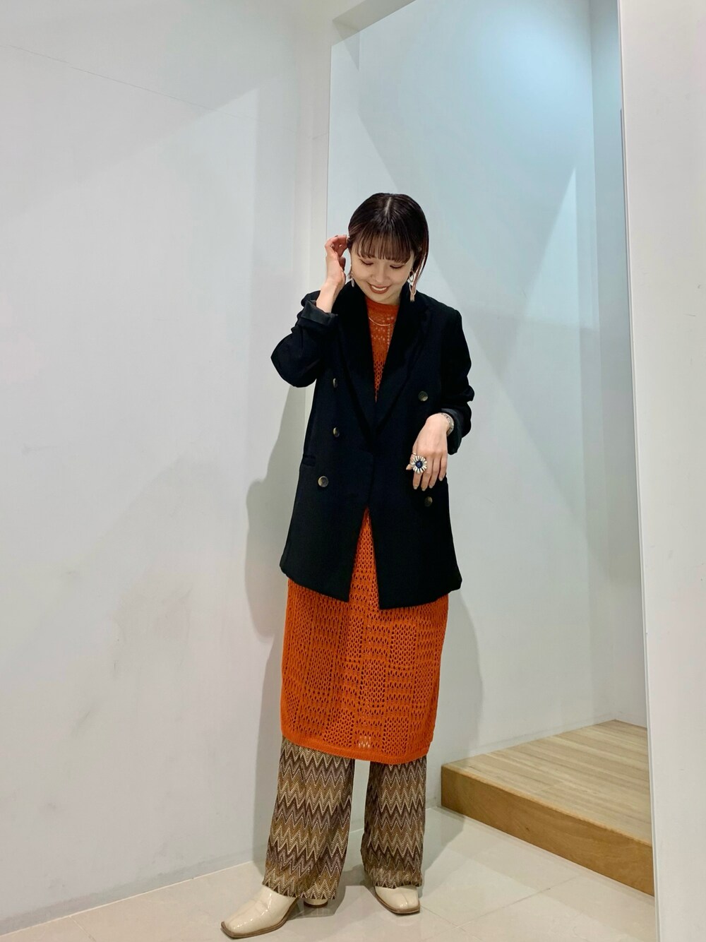 ブラック系のテーラードジャケット、オレンジ系のベスト、ブラウン系のその他パンツを着用したレディースの春コーディネートの1枚目の写真