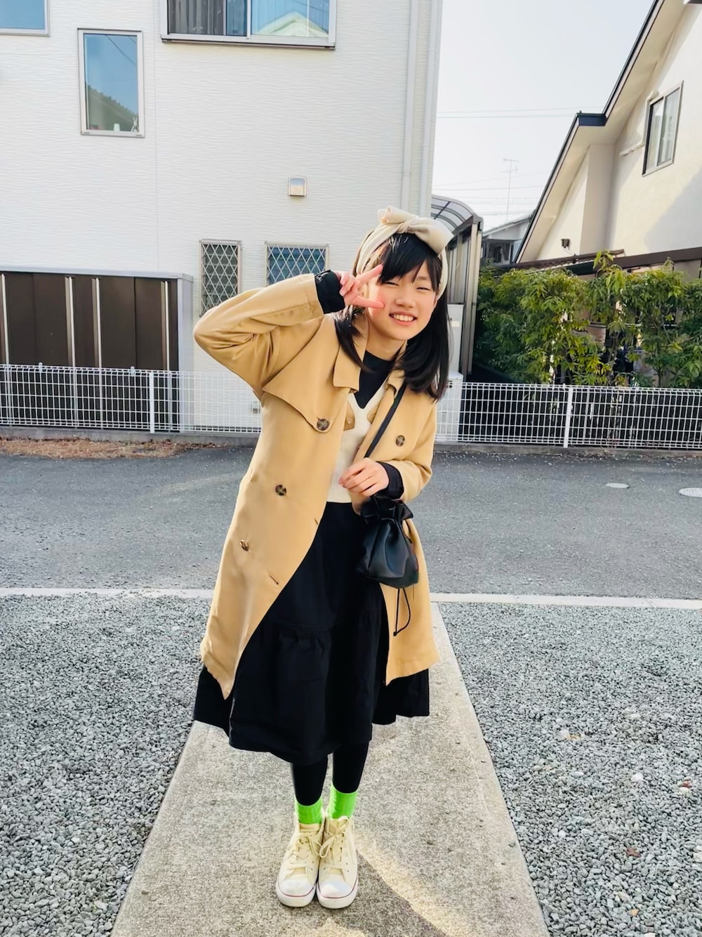 ベージュ系のトレンチコート、ブラック系のハンドバッグ、ブラック系のワンピースを着用したキッズの春コーディネートの1枚目の写真