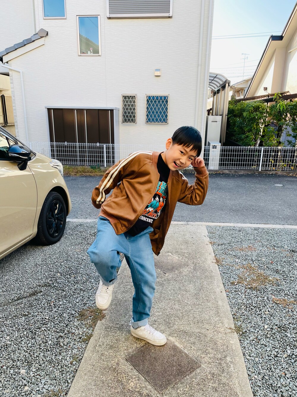 ブラウン系のノーカラージャケット、ブルー系のデニムパンツ、ホワイト系のスニーカーを着用したキッズの秋コーディネートの1枚目の写真