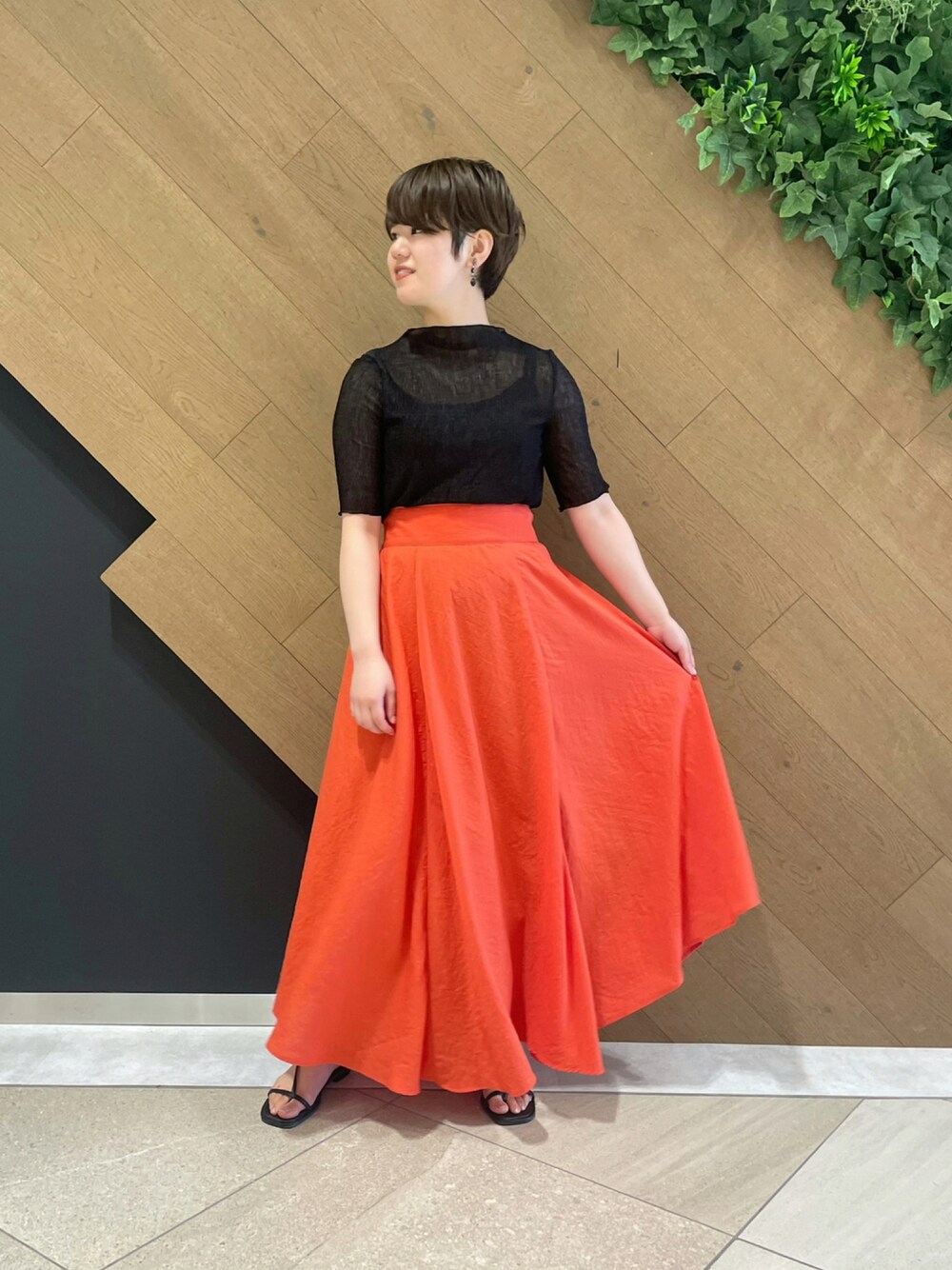 ブラック系のアンサンブル、レッド系のスカート、ブラック系のサンダルを着用したレディースの夏コーディネートの1枚目の写真