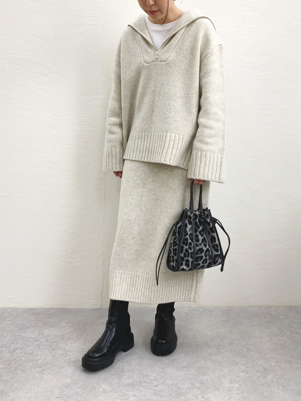 ホワイト系のニット/セーター、ホワイト系のスカート、ブラック系のブーツを着用したレディースの秋コーディネートの1枚目の写真