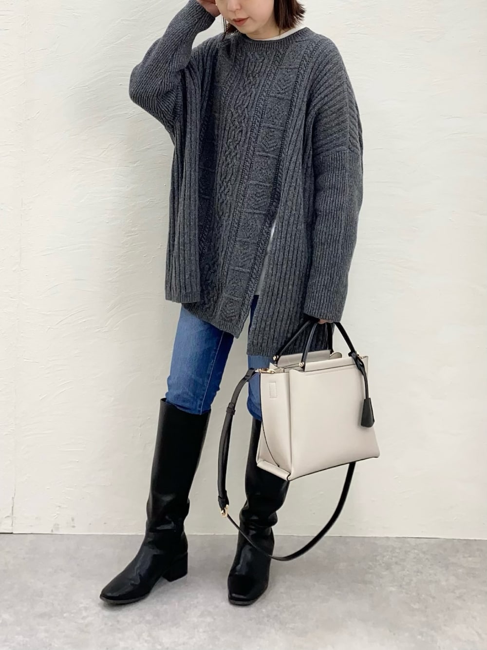 グレー系のニット/セーター、グレー系のハンドバッグ、ブルー系のデニムパンツを着用したレディースの冬コーディネートの1枚目の写真