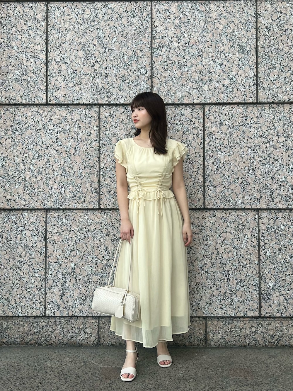 イエロー系のワンピース、ホワイト系のボストンバッグ、ホワイト系のサンダルを着用したレディースの夏コーディネートの1枚目の写真