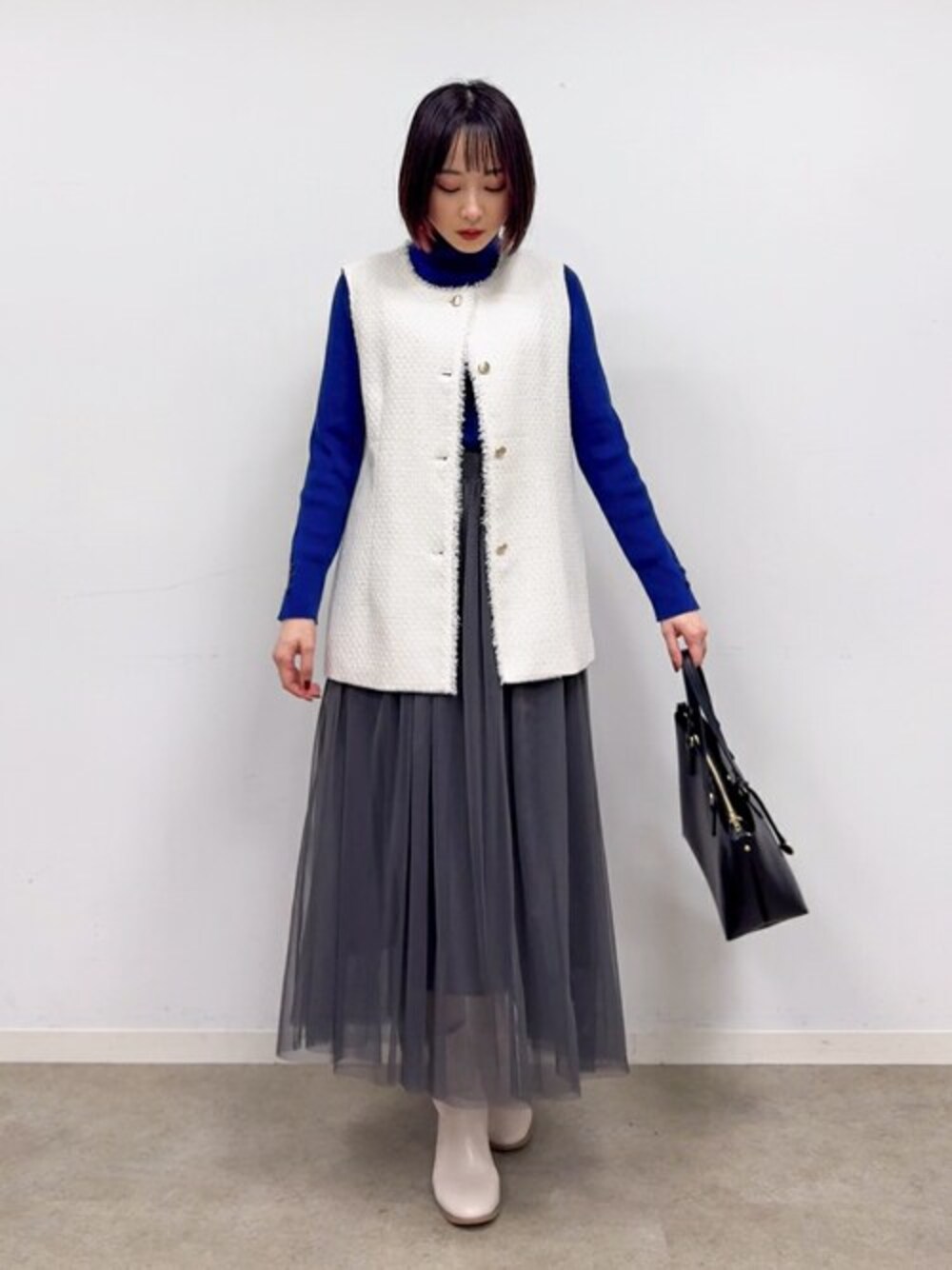 ベージュ系のベスト、ブルー系のニット/セーター、グレー系のスカートを着用したレディースの冬コーディネートの1枚目の写真