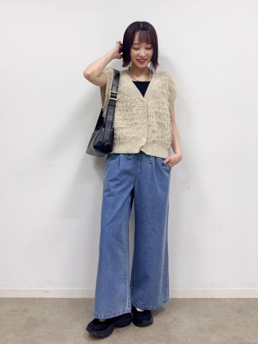 ベージュ系のベスト、ブルー系のデニムパンツ、ブラック系のスニーカーを着用したレディースの秋コーディネートの1枚目の写真