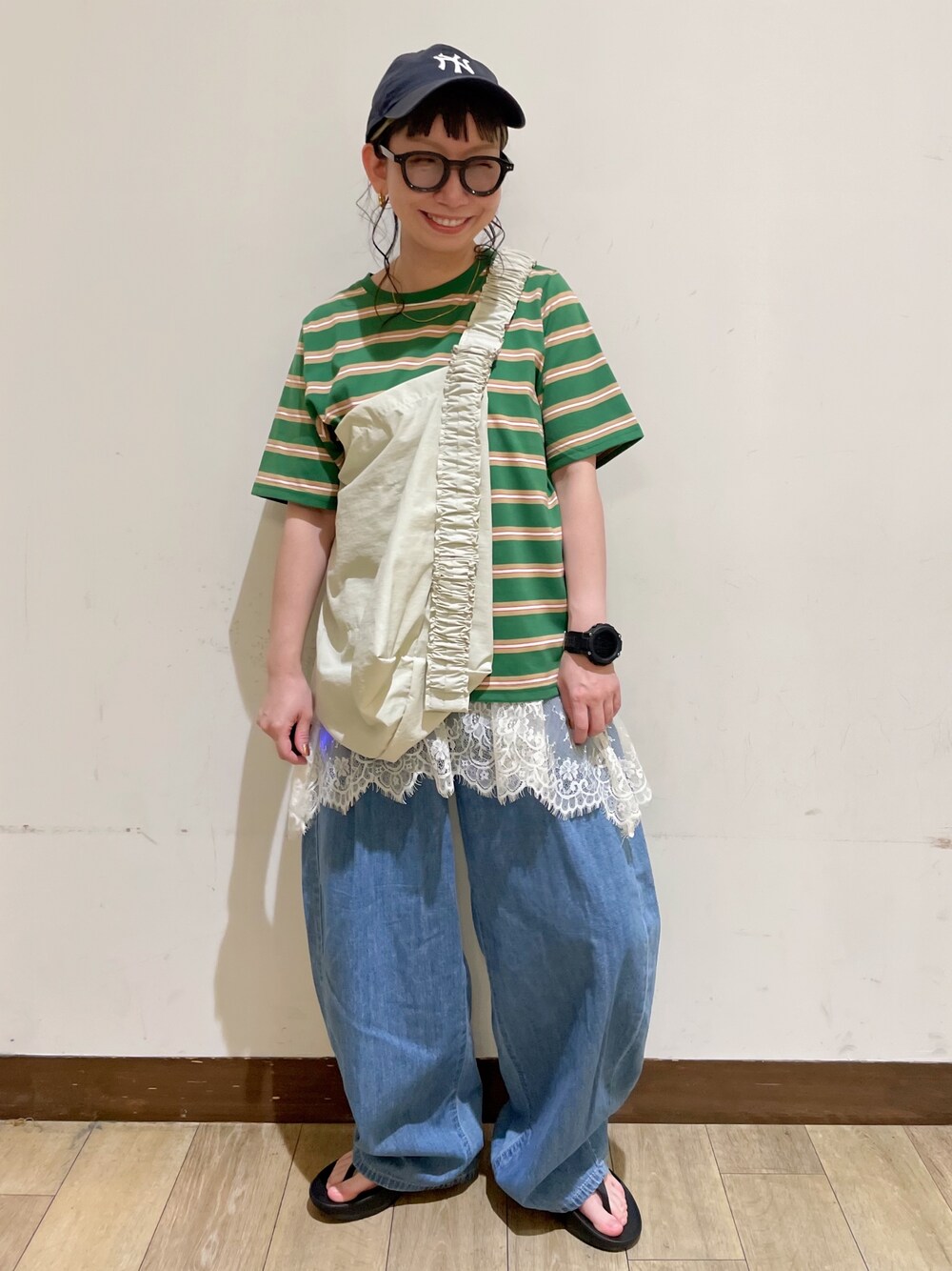 ブルー系のデニムパンツ、ベージュ系のショルダーバッグ、ブラック系のサンダルを着用したレディースの夏コーディネートの1枚目の写真