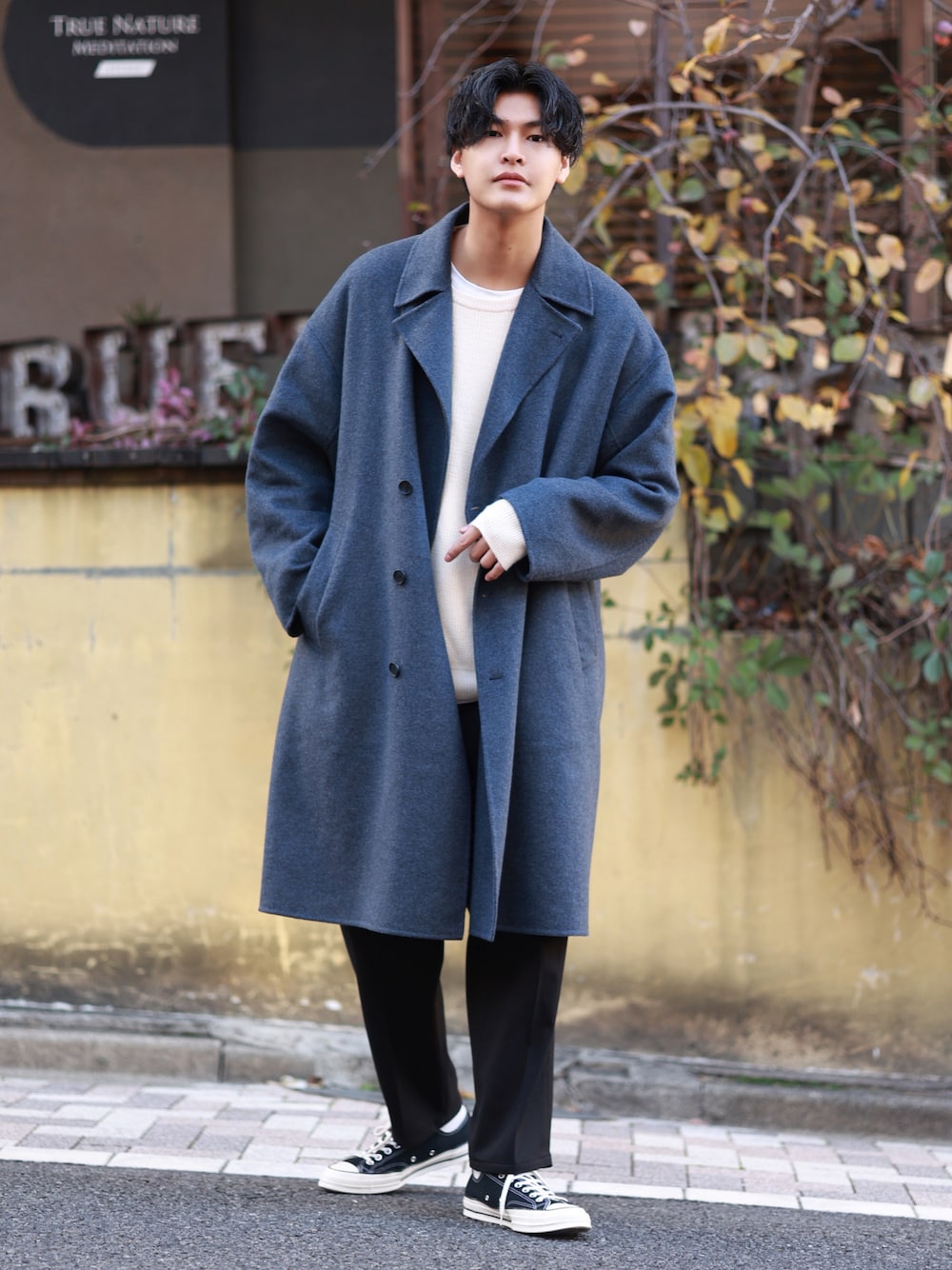 ブルー系のトレンチコート、ホワイト系のニット/セーター、ブラック系のスラックスを着用したメンズの冬コーディネートの1枚目の写真