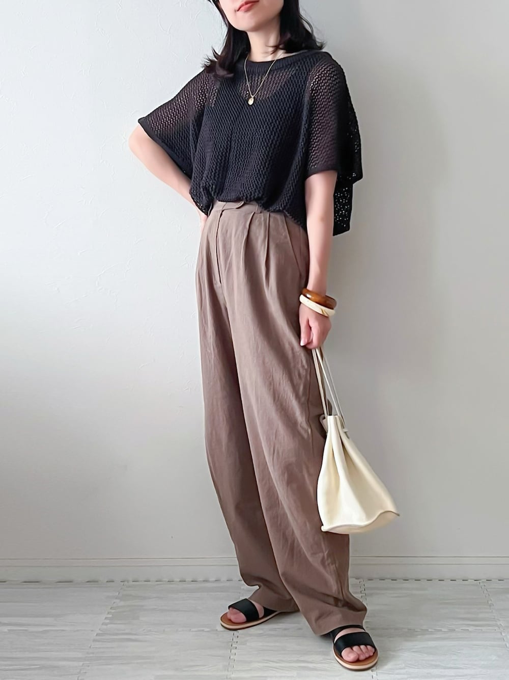 グレー系のニット/セーター、ブラウン系のスラックス、ベージュ系のショルダーバッグを着用したレディースの夏コーディネートの1枚目の写真