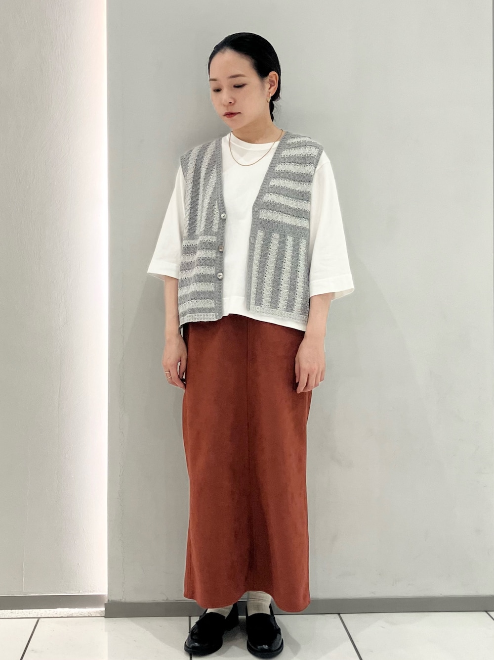 ホワイト系のTシャツ/カットソー、グレー系のベスト、オレンジ系のスカートを着用したレディースの秋コーディネートの1枚目の写真
