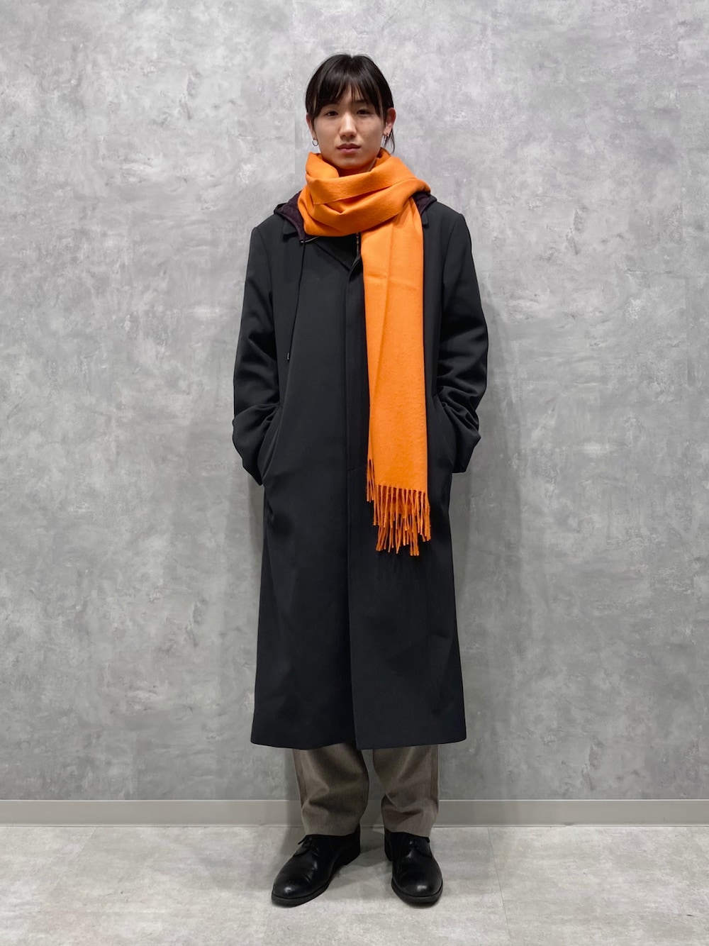 ブラック系のステンカラーコート、イエロー系のスラックス、オレンジ系のマフラーを着用したメンズの秋コーディネートの1枚目の写真