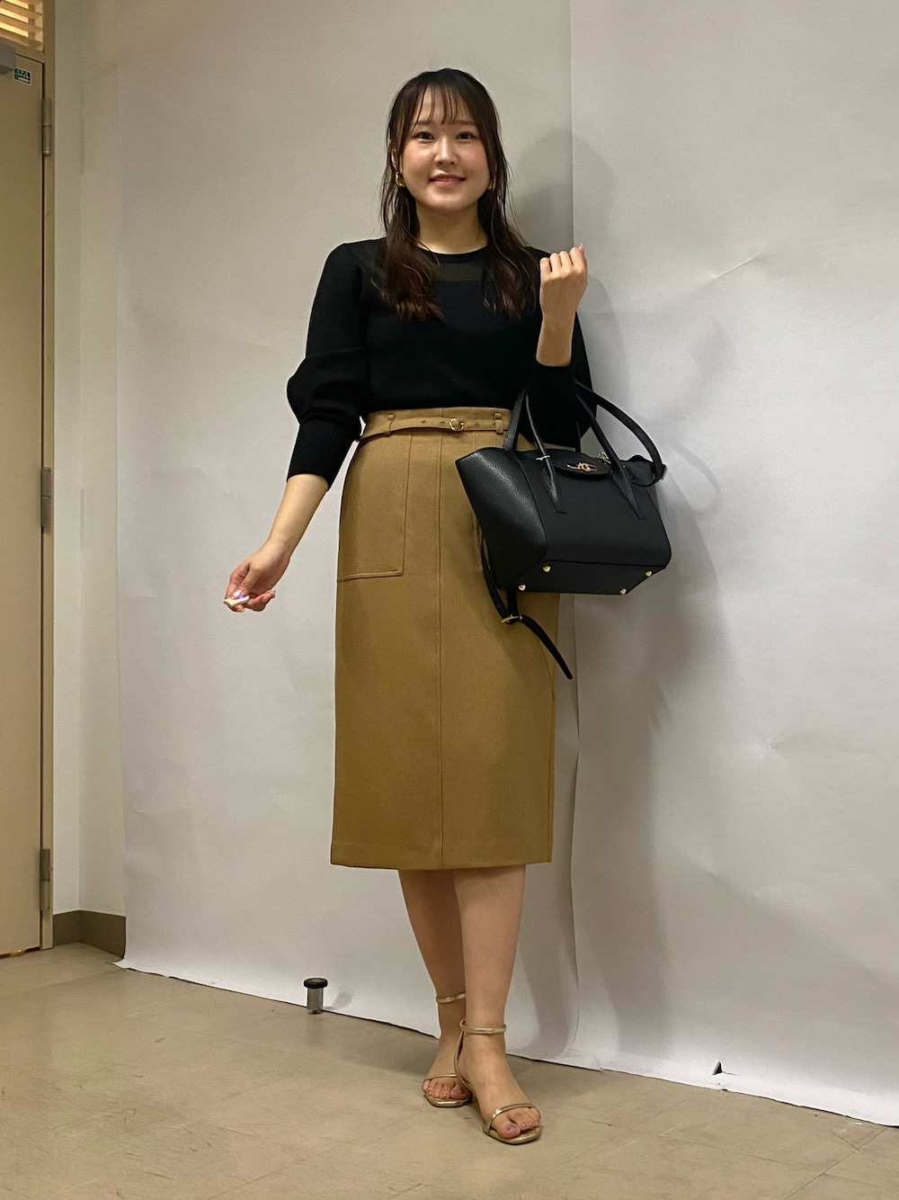 イエロー系のスカート、ブラック系のショルダーバッグ、ブラック系のニット/セーターを着用したレディースの秋コーディネートの1枚目の写真