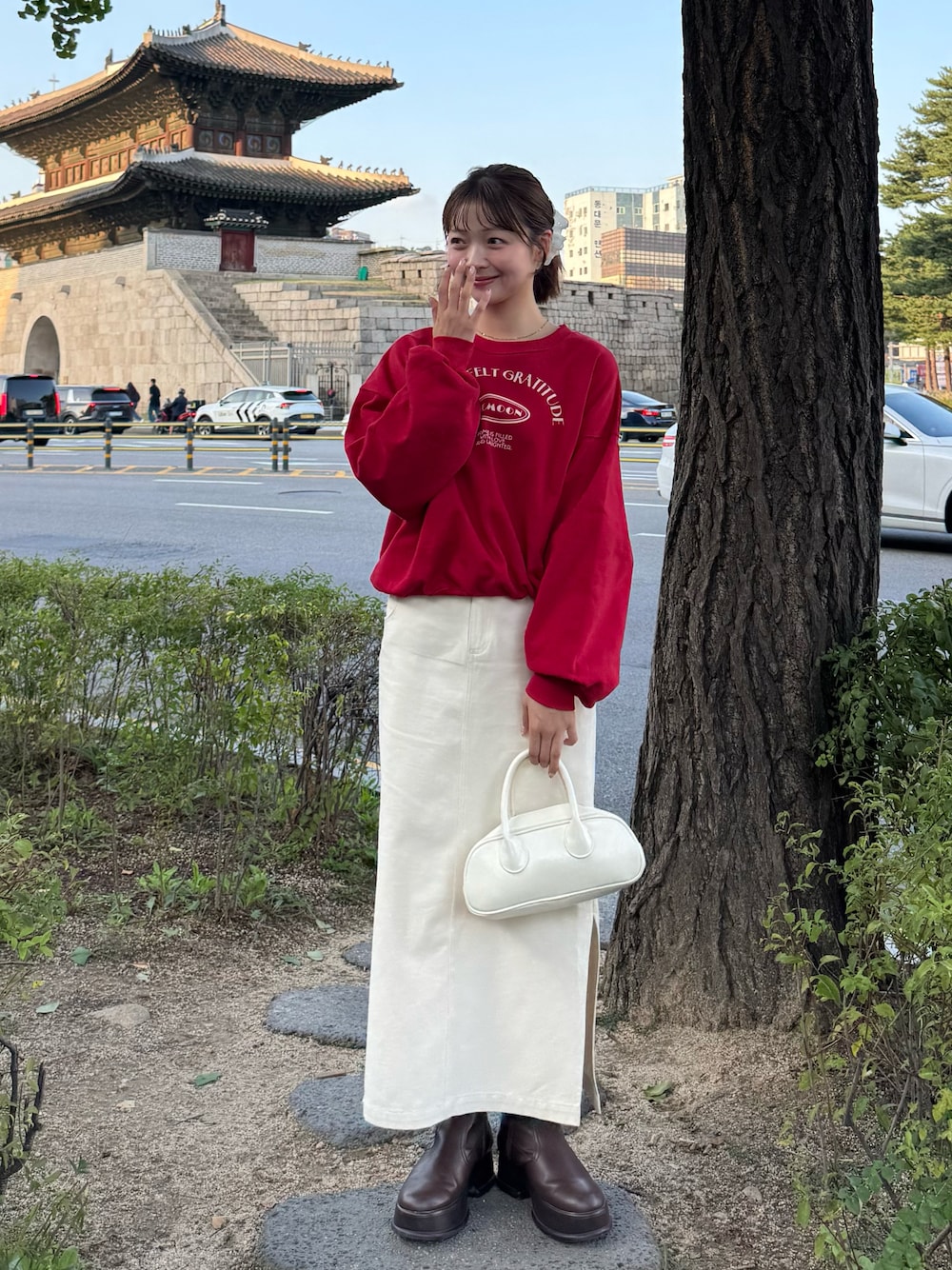 レッド系のスウェット、ベージュ系のスカート、ブラウン系のブーツを着用したレディースの秋コーディネートの1枚目の写真