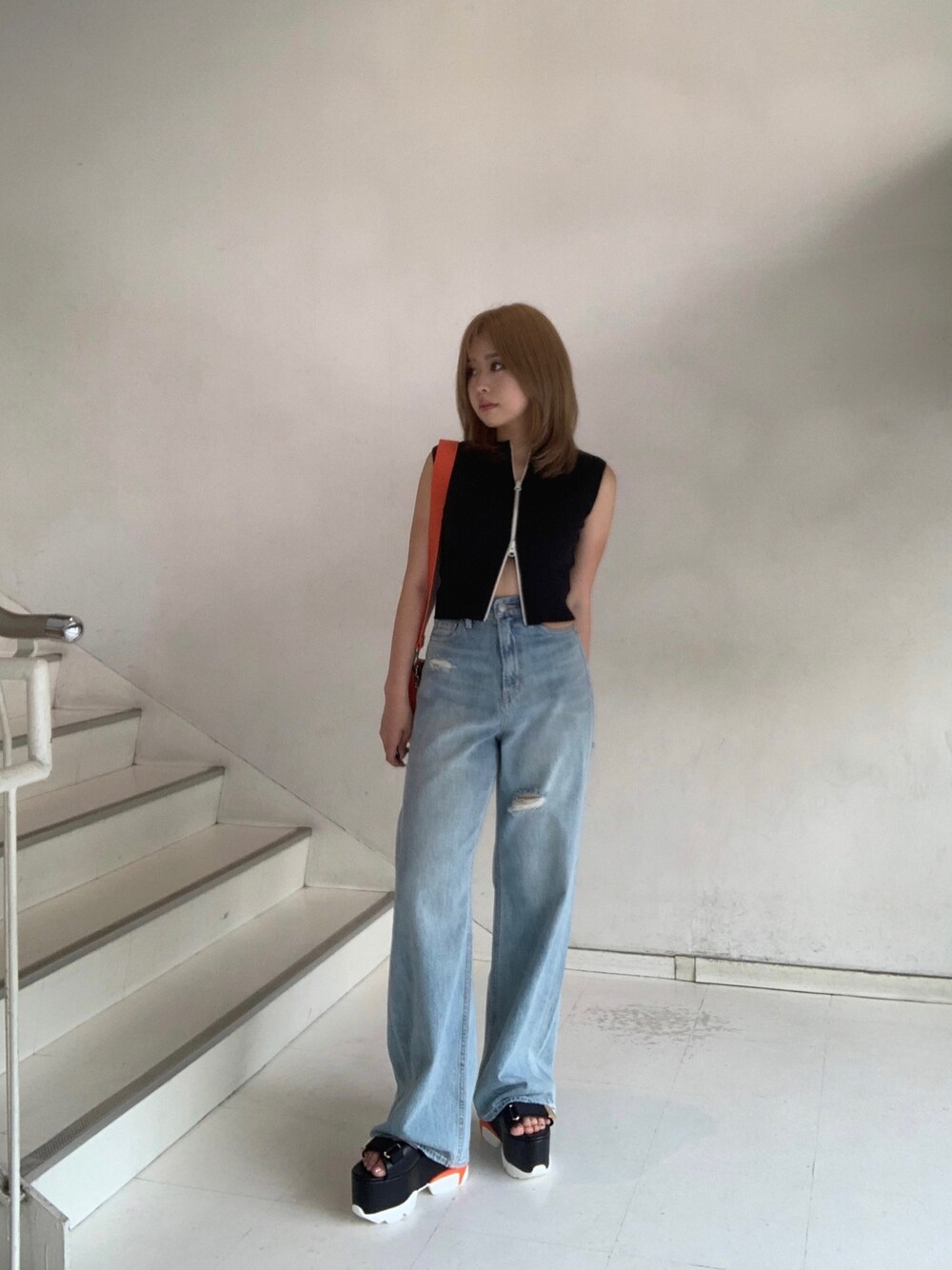 ブラック系のタンクトップ、ブルー系のデニムパンツ、オレンジ系のショルダーバッグを着用したレディースの夏コーディネートの1枚目の写真