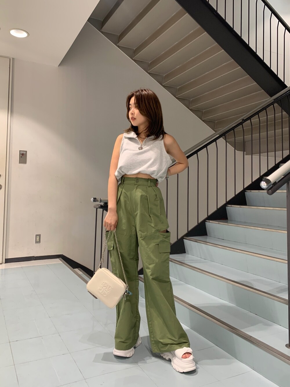 グレー系のタンクトップ、グリーン系のカーゴパンツ、ホワイト系のショルダーバッグを着用したレディースの春コーディネートの1枚目の写真