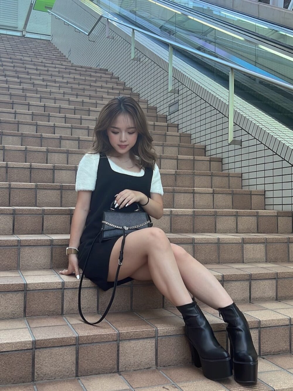 ホワイト系のニット/セーター、ブラック系のハンドバッグ、ブラック系のブーツを着用したレディースの夏コーディネートの1枚目の写真