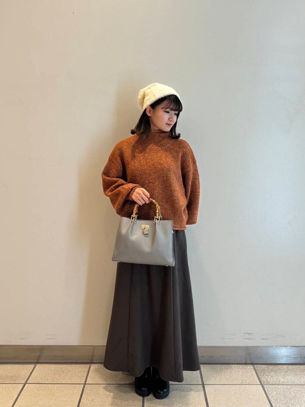 グレー系のハンドバッグ、グレー系のスカート、オレンジ系のニット/セーターを着用したレディースの冬コーディネートの1枚目の写真