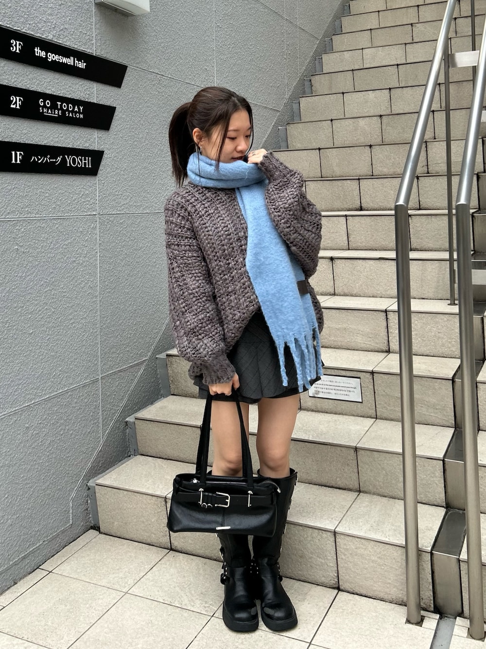 グレー系のニット/セーター、ブラック系のスカート、ブラック系のショルダーバッグを着用したレディースの秋コーディネートの1枚目の写真