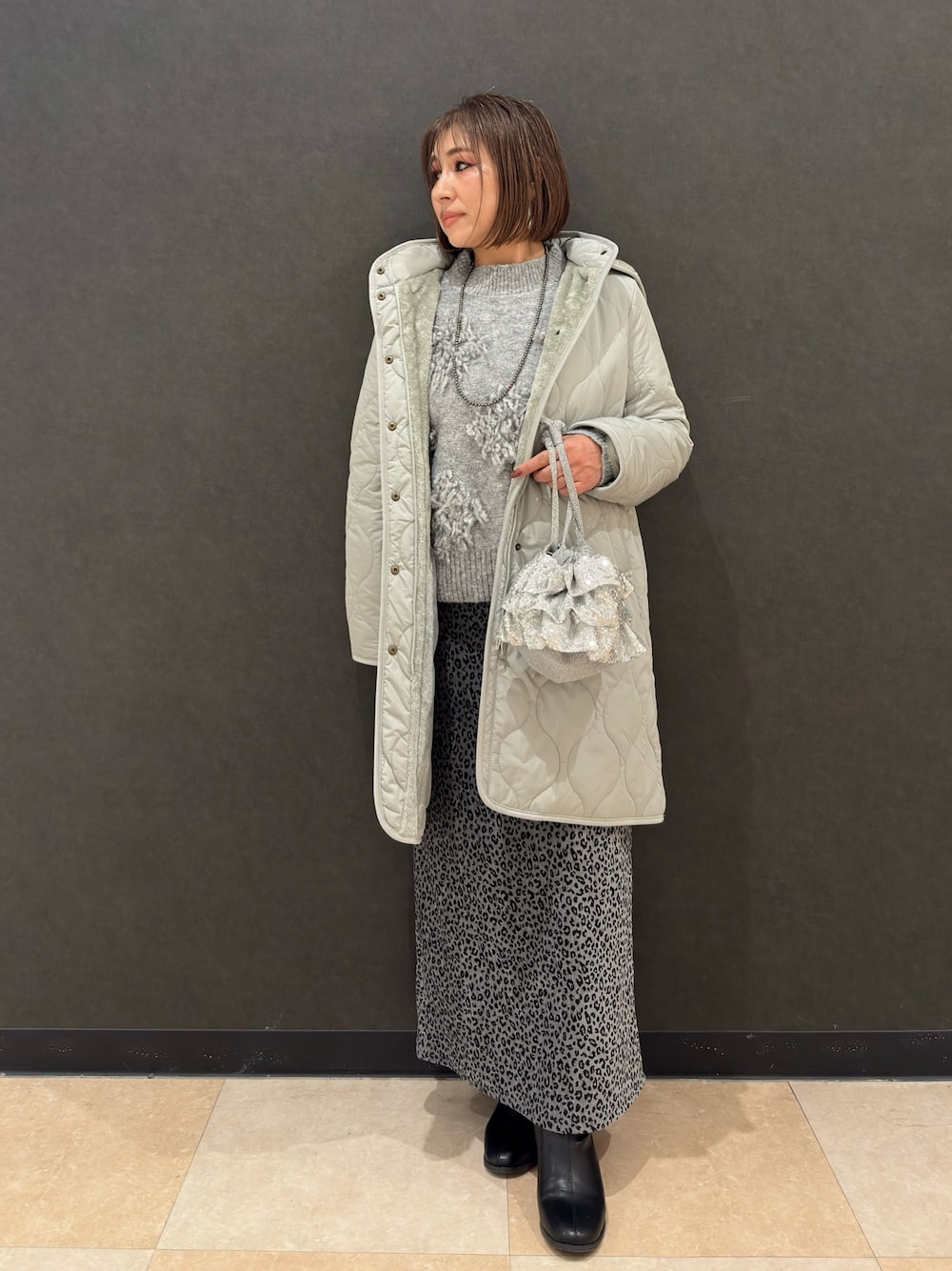 ブラック系のブーツ、シルバー系のショルダーバッグ、グレー系のスカートを着用したレディースの冬コーディネートの1枚目の写真