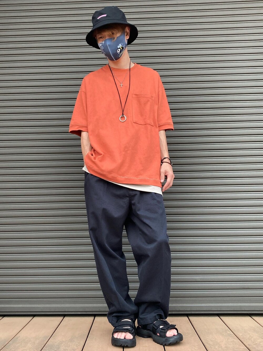 オレンジ系のTシャツ/カットソー、ブラック系のチノパンツ、ブラック系のサンダルを着用したメンズの夏コーディネートの1枚目の写真