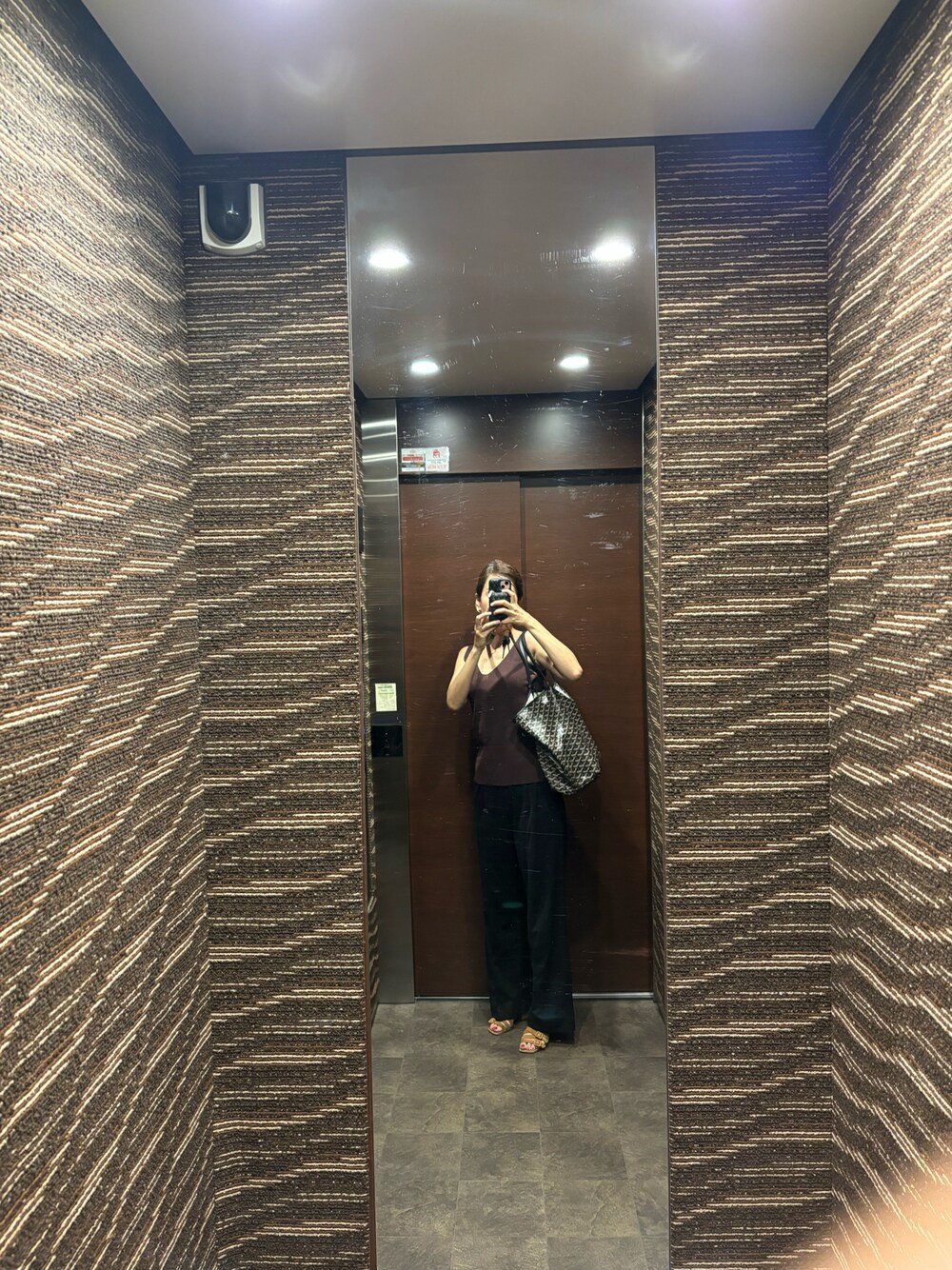 ブラック系のスラックス、ブラック系のトートバッグ、ブラウン系のタンクトップを着用したレディースの夏コーディネートの1枚目の写真