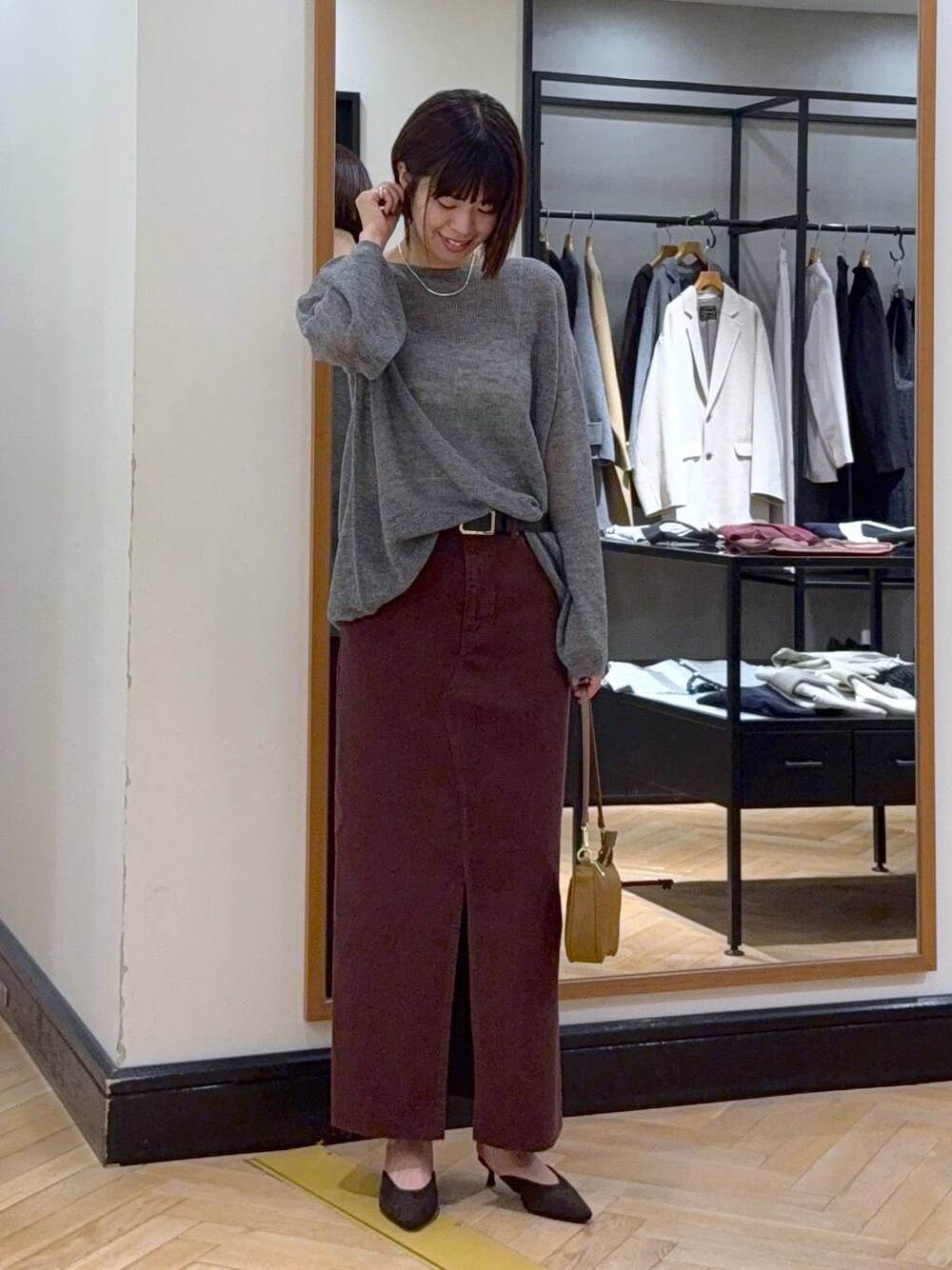 グレー系のニット/セーター、レッド系のデニムスカート、ブラウン系のパンプスを着用したレディースの秋コーディネートの1枚目の写真