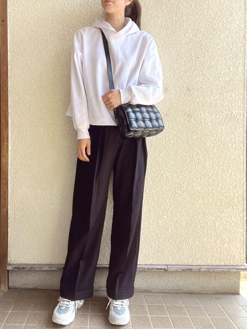 ブラック系のスラックス、ブラック系のショルダーバッグ、ホワイト系のパーカーを着用したレディースの春コーディネートの1枚目の写真