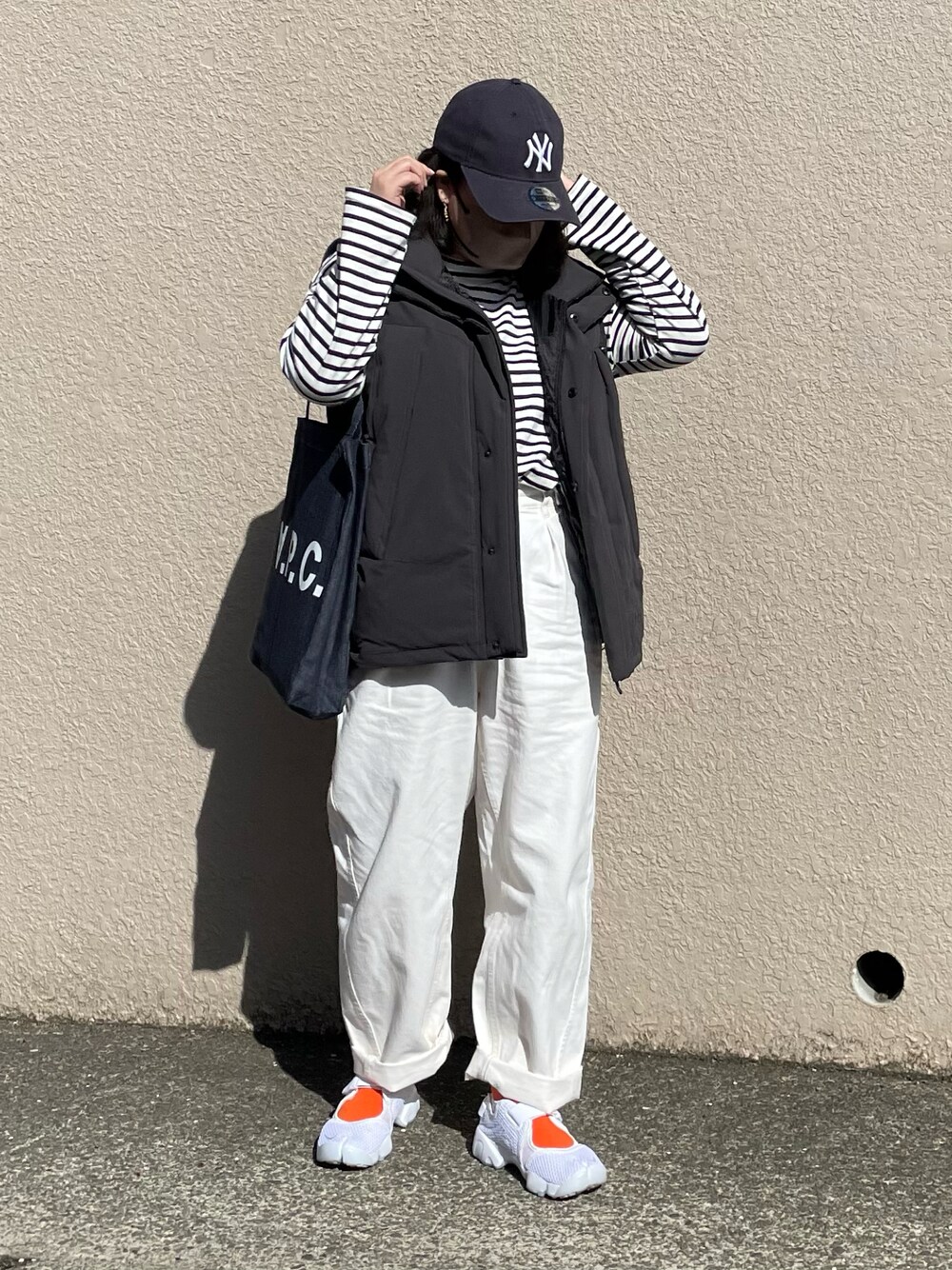 ブラック系のダウンベスト、ブルー系のトートバッグ、ホワイト系のパンツを着用したレディースの春コーディネートの1枚目の写真