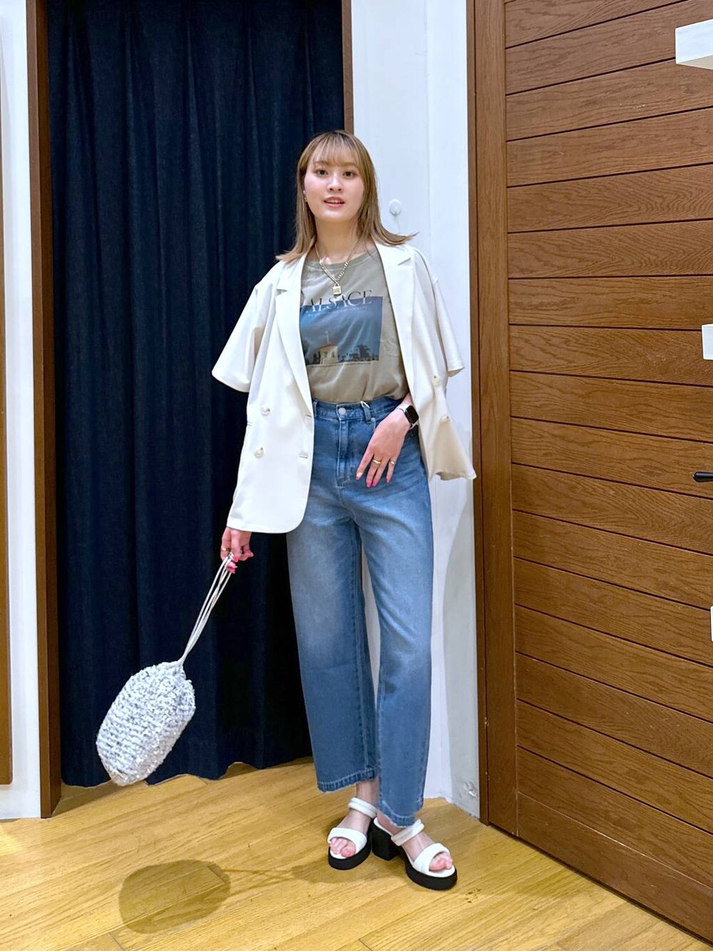 シルバー系のハンドバッグ、ホワイト系のテーラードジャケット、ブルー系のデニムパンツを着用したレディースの夏コーディネートの1枚目の写真