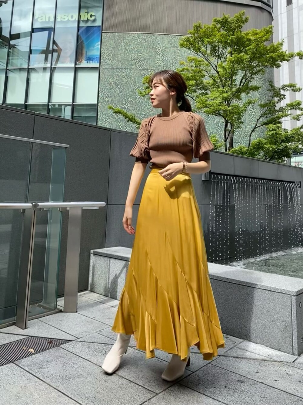 イエロー系のスカート、ホワイト系のその他シューズ、ブラウン系のニット/セーターを着用したレディースの夏コーディネートの1枚目の写真