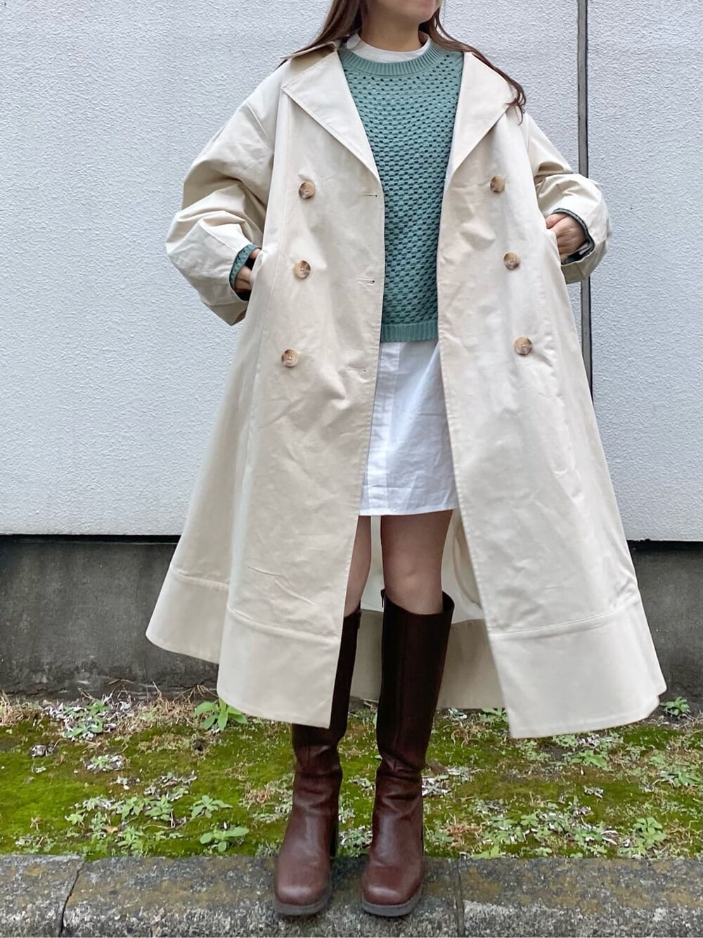 ブラウン系のブーツ、ブルー系のニット/セーター、ホワイト系のトレンチコートを着用したレディースの冬コーディネートの1枚目の写真