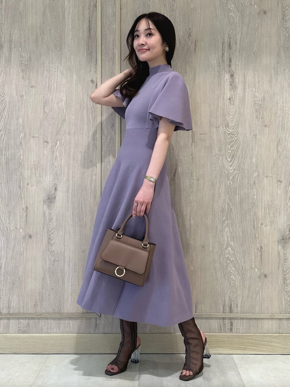 ブラウン系のハンドバッグ、ブラウン系のブーツ、パープル系のワンピースを着用したレディースの春コーディネートの1枚目の写真