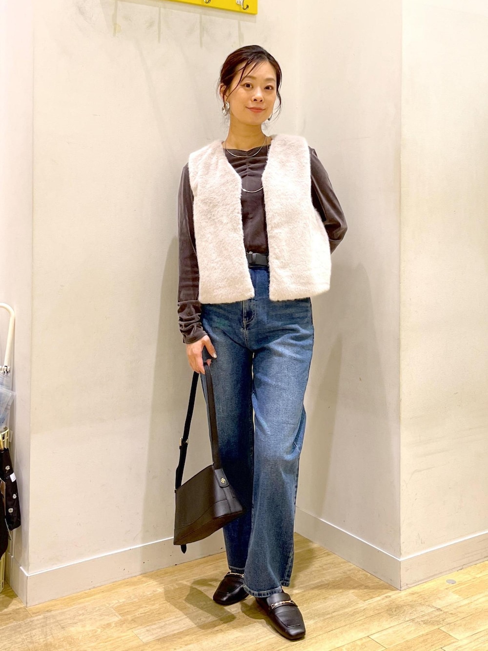 ブルー系のデニムパンツ、ブラック系のショルダーバッグ、ベージュ系のベストを着用したレディースの秋コーディネートの1枚目の写真
