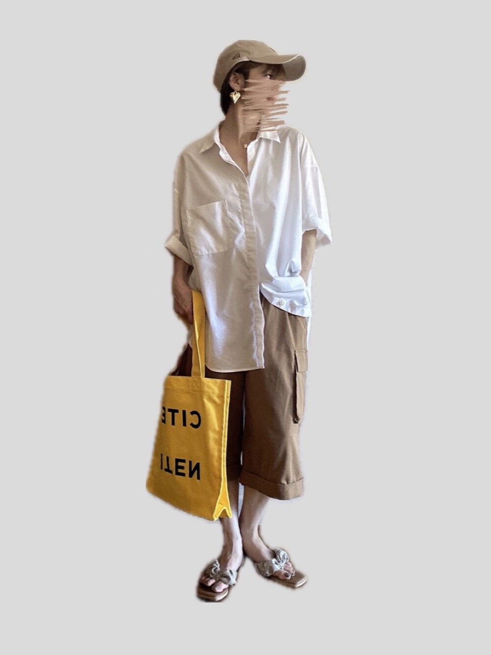 イエロー系のトートバッグ、ベージュ系のパンツ、ゴールド系のサンダルを着用したレディースの夏コーディネートの1枚目の写真