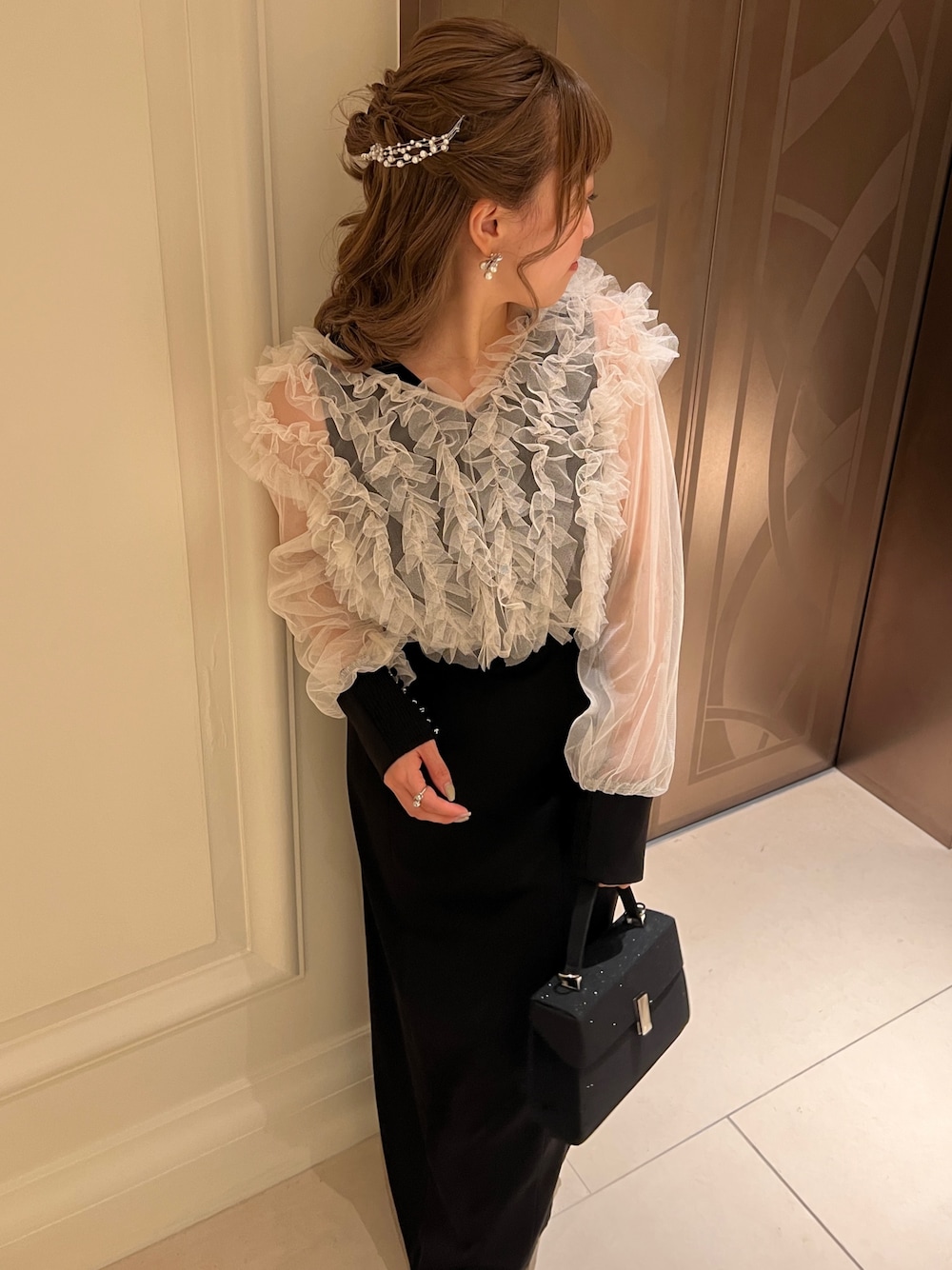 ブラック系のドレス、ブラック系のハンドバッグ、ゴールド系のヘアピンを着用したレディースの春コーディネートの1枚目の写真