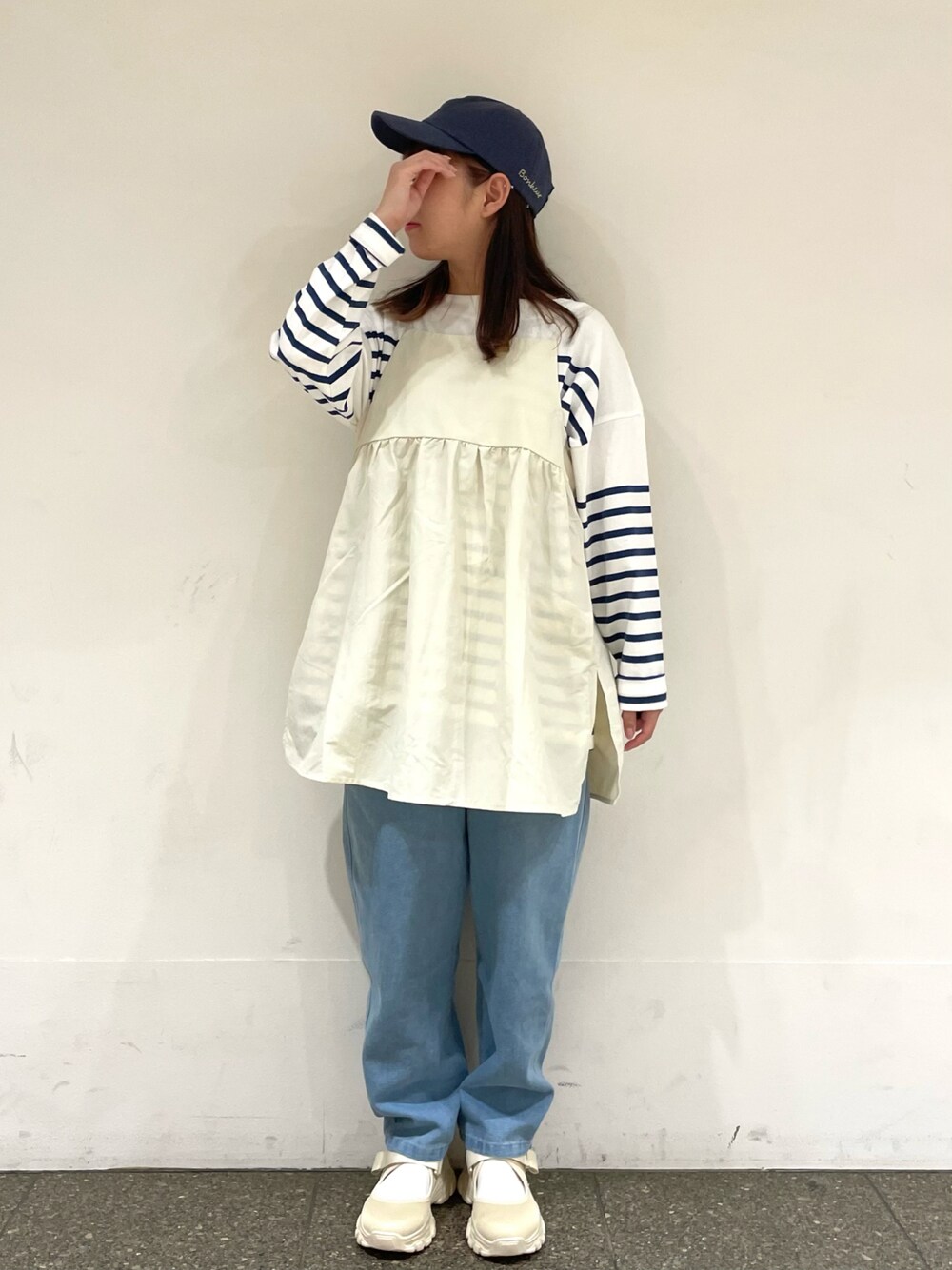ベージュ系のスニーカー、ホワイト系のチュニック、ブルー系のデニムパンツを着用したレディースの春コーディネートの1枚目の写真