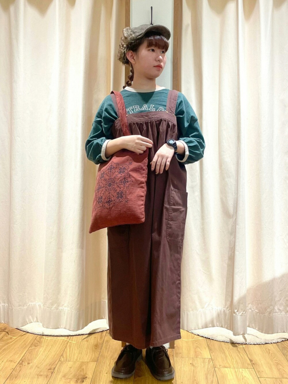 グリーン系のTシャツ/カットソー、ブラウン系のジャンパースカート、レッド系のトートバッグを着用したレディースの秋コーディネートの1枚目の写真