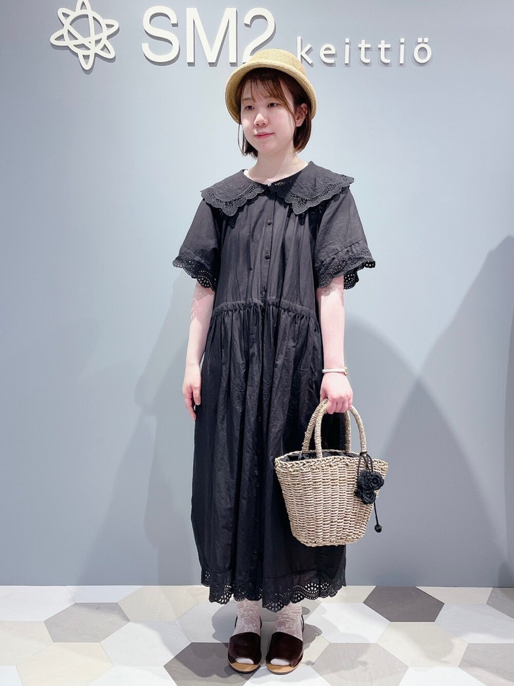 ブラック系のワンピース、ベージュ系のかごバッグ、ブラウン系のサンダルを着用したレディースの夏コーディネートの1枚目の写真