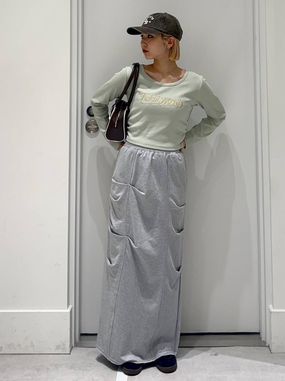 グレー系のスカート、グリーン系のTシャツ/カットソー、ブラウン系のボストンバッグを着用したレディースの春コーディネートの1枚目の写真