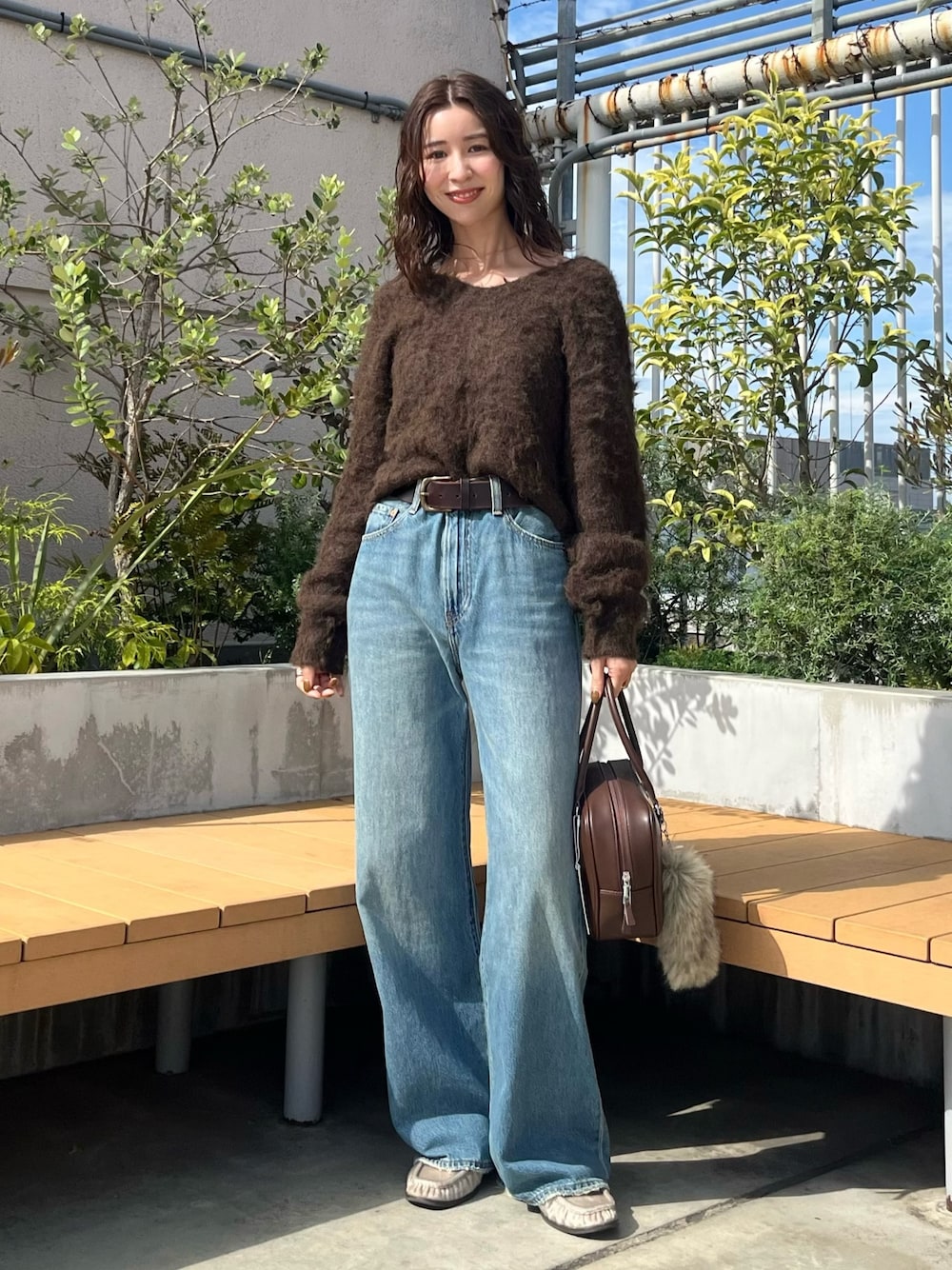 ブラウン系のニット/セーター、ブルー系のデニムパンツ、ブラウン系のハンドバッグを着用したレディースの秋コーディネートの1枚目の写真